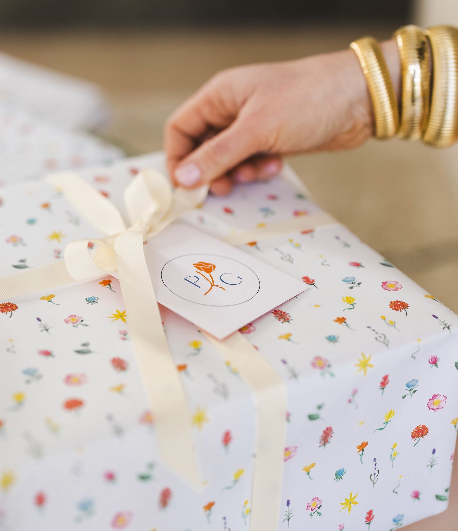 Hand tying a bow on a gift wrapped in colorful paper with a visible brand logo.