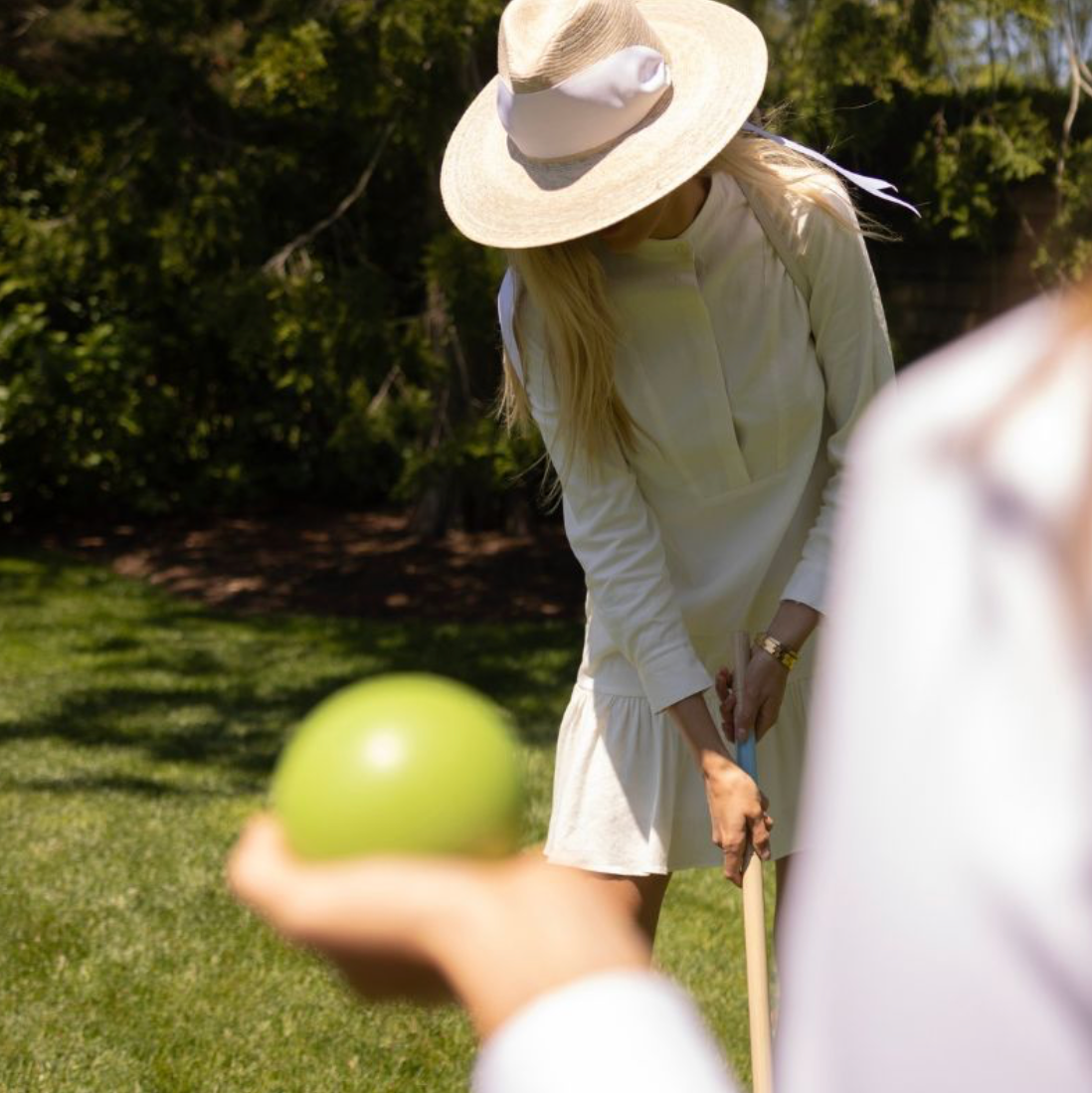 Person playing croquet on a grassy lawn with a green ball and mallet.